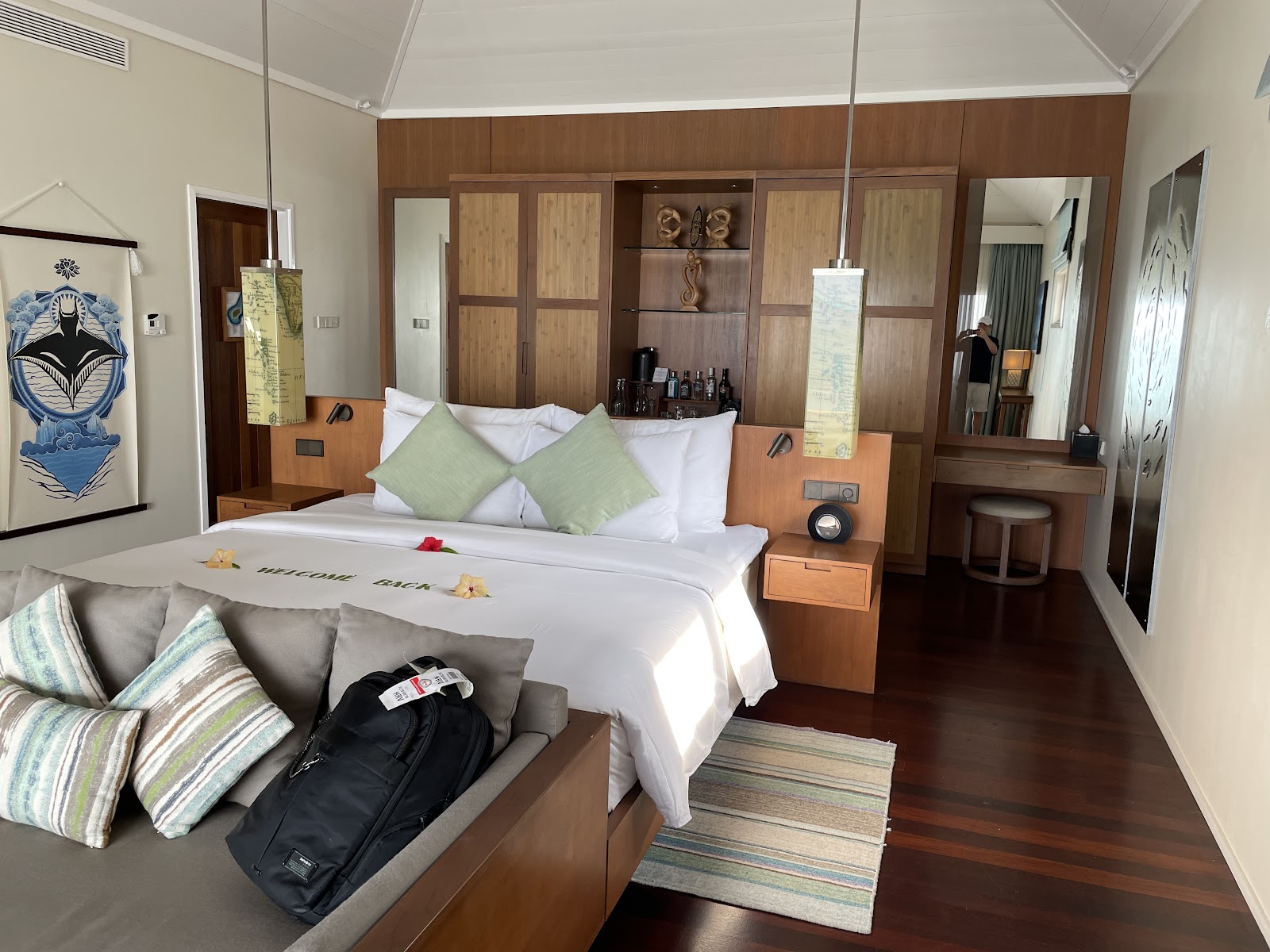 Resort bedroom with king bed, green accent pillows, wood cabinetry, sitting area with gray sofa, and dark wood flooring throughout.