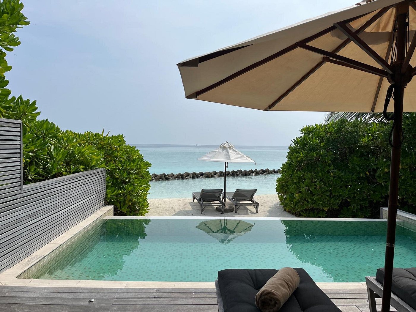 Overwater bungalow at Hurawalhi Island Resort with wooden deck, lounge chairs, white umbrella, and sandy beach platform in turquoise lagoon.
