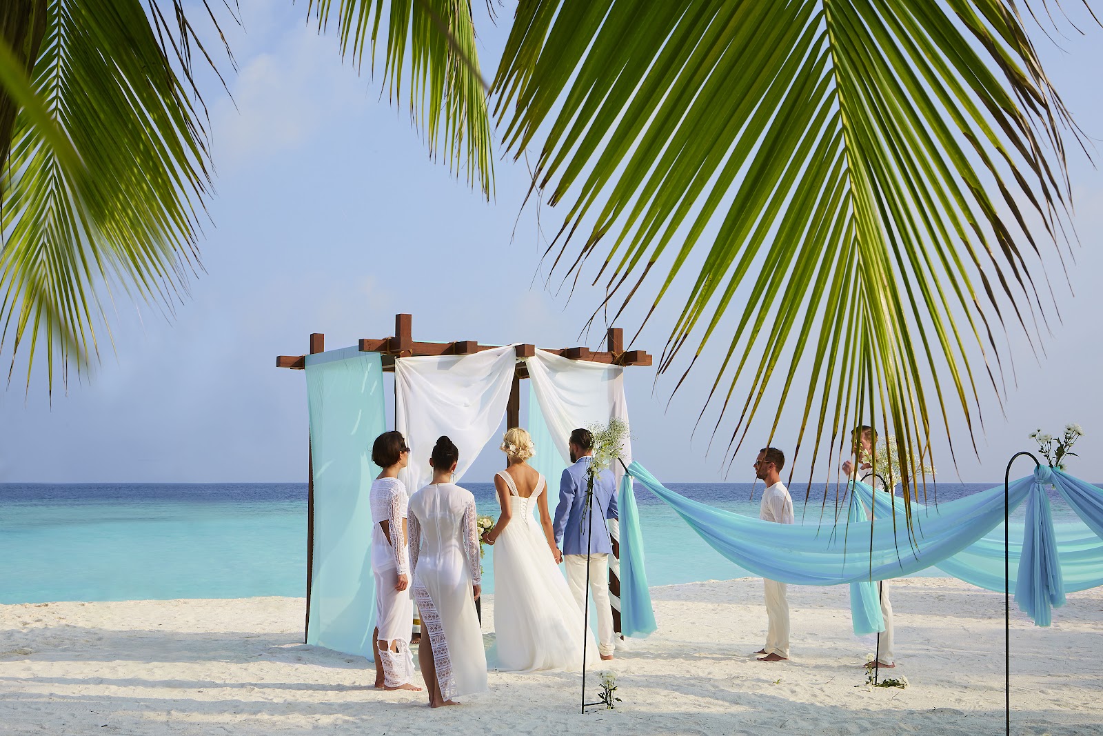 Overwater villa deck at sunset with soaking tub, lounge chairs, umbrella, and ocean view at Hurawalhi Island Resort.