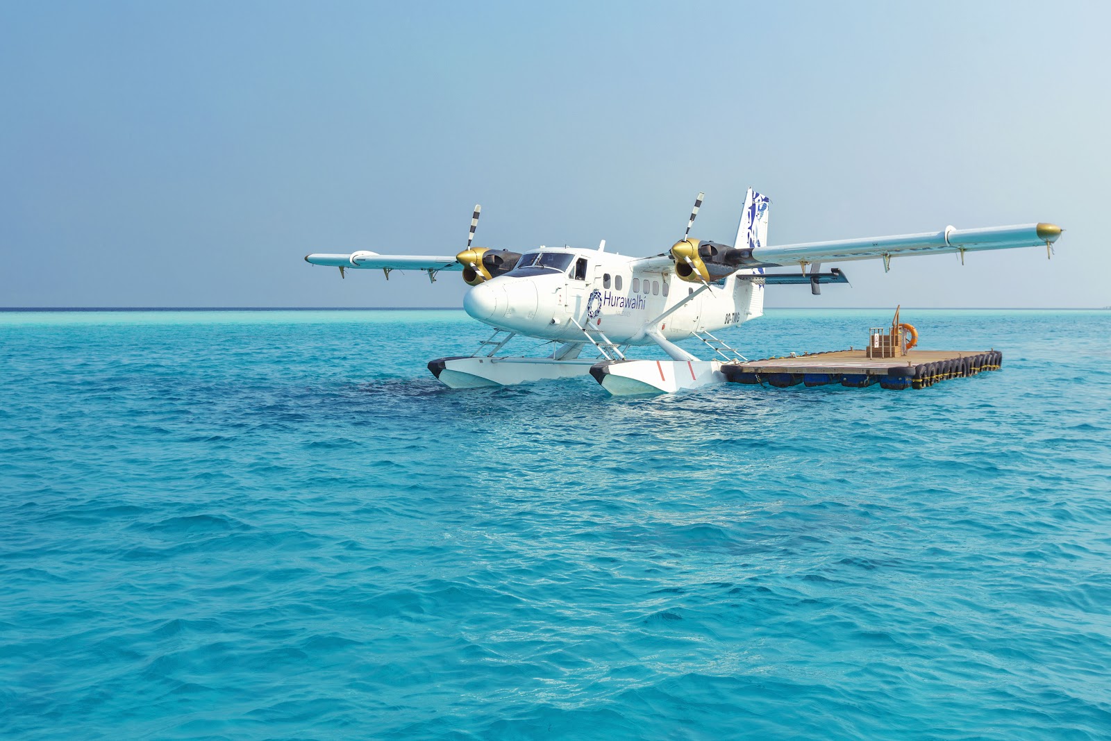 White seaplane with yellow engines moored in turquoise water next to a wooden dock.