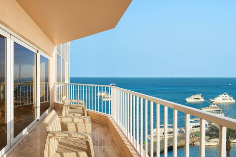 Oceanfront balcony at Hurghada Marriott Beach Resort with lounge chairs, white railing, and view of blue water and moored boats.
