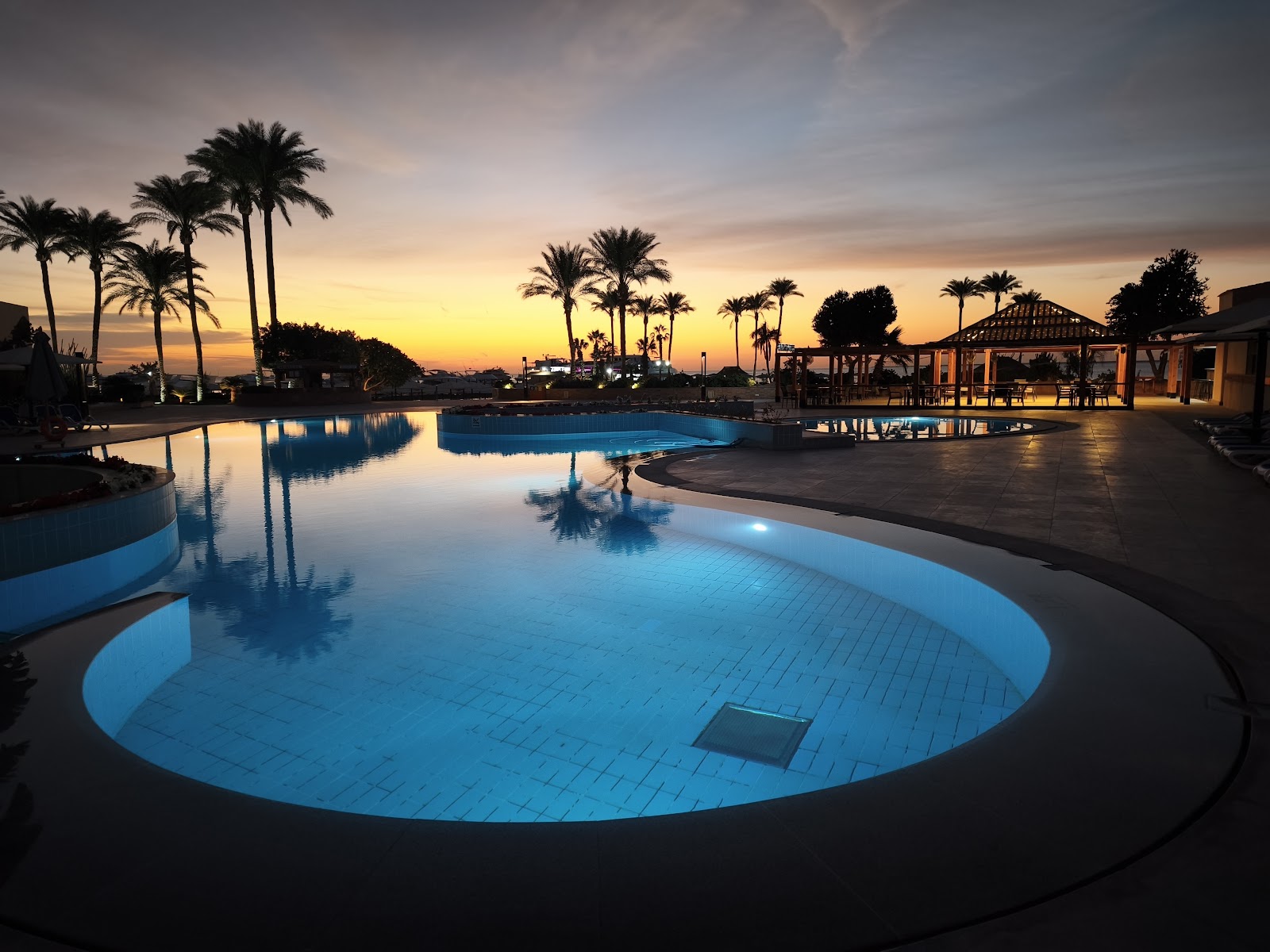 Illuminated pools and palm trees at dusk with beachfront pavilions and lounge areas at Hurghada Marriott Beach Resort.