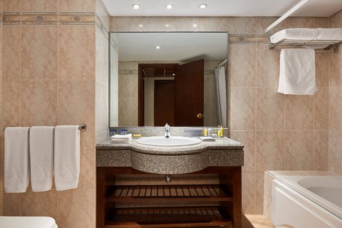 Bathroom with beige tile walls, curved sink vanity with dark wood shelving, large mirror, and white towels on rack beside bathtub.
