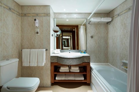 Bathroom with beige tile walls, white toilet on left, wooden vanity with sink and mirror, bathtub on right, and towel rack at Hurghada Marriott Beach Resort.