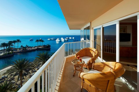 Wooden lounge chairs on a balcony overlooking the Red Sea and palm-lined beach at Hurghada Marriott Beach Resort.