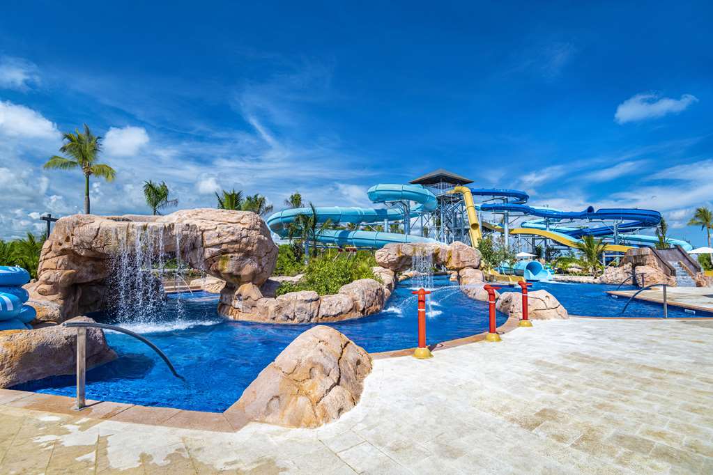 Water park with blue pools, artificial rock formations, waterfall, and multiple slides under clear sky at Hyatt Zilara Cap Cana.