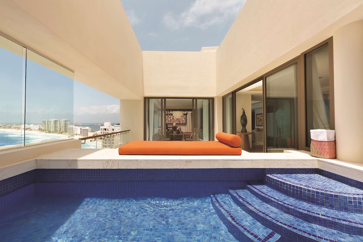 Private pool on a high-rise balcony with ocean and beach coastline visible through floor-to-ceiling windows.