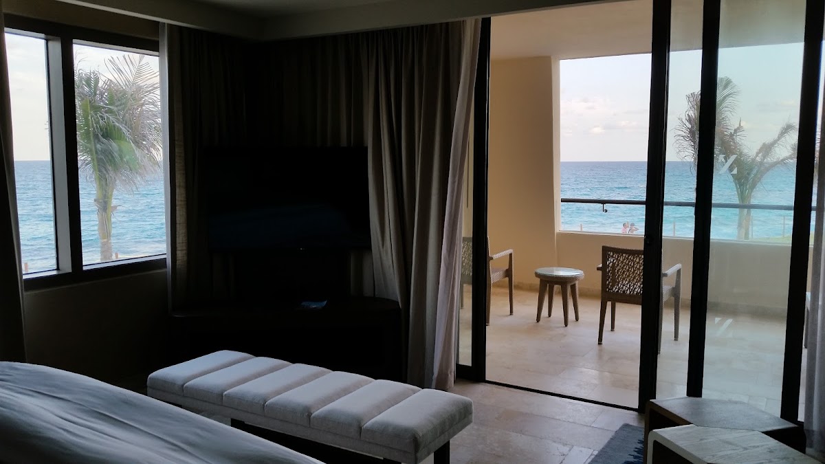 Beachfront suite at Hyatt Ziva Cancún with ocean views through floor-to-ceiling windows, black canopy bed, and terrace seating overlooking the turquoise Caribbean Sea.