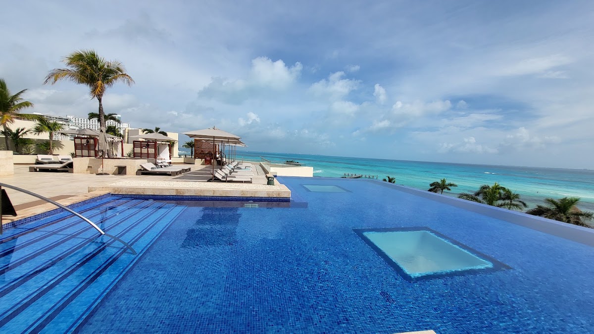 Infinity pool with swim lanes overlooking turquoise Caribbean water, palm trees, and beach cabanas at Hyatt Ziva Cancún.