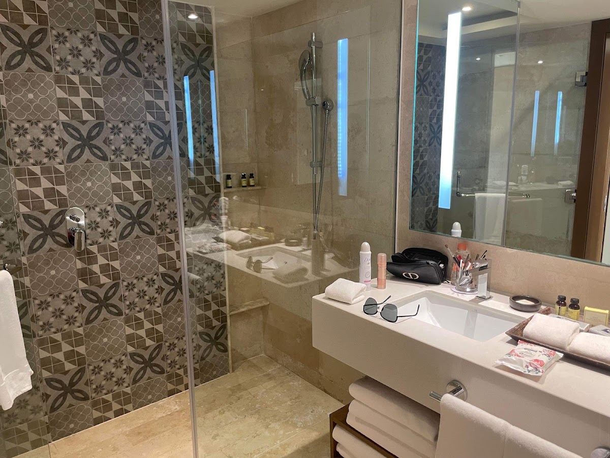 Bathroom with walk-in shower featuring patterned tile walls, illuminated mirror, white countertop sink, and toiletries at Hyatt Ziva Cancún.