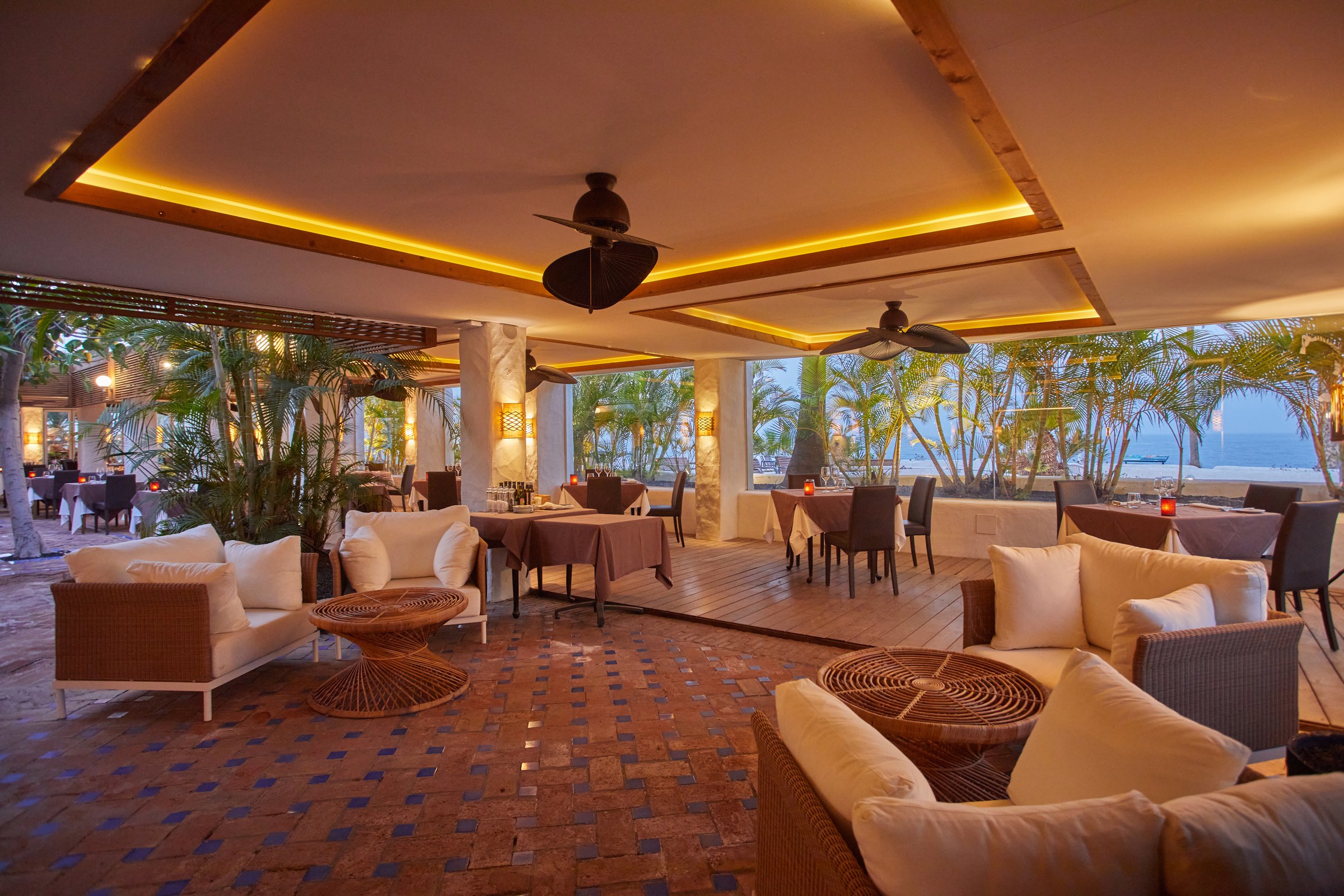 Babbo open-air restaurant and lounge with wicker sofas, set tables and the sea beyond.