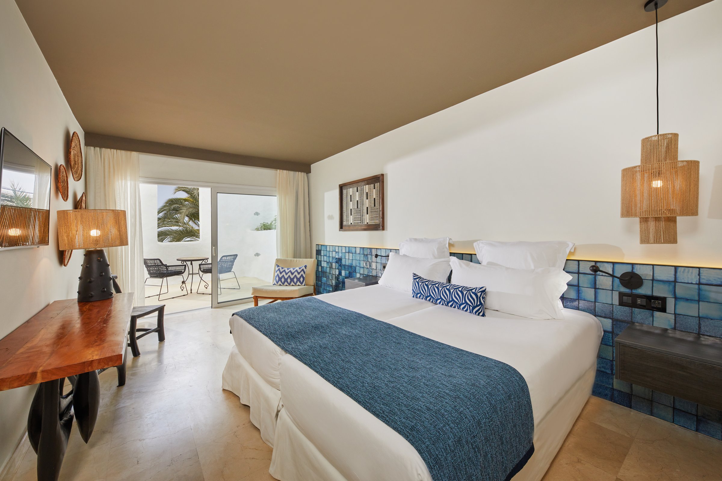 Junior suite with blue-tiled headboard wall, balcony doors and palm views.