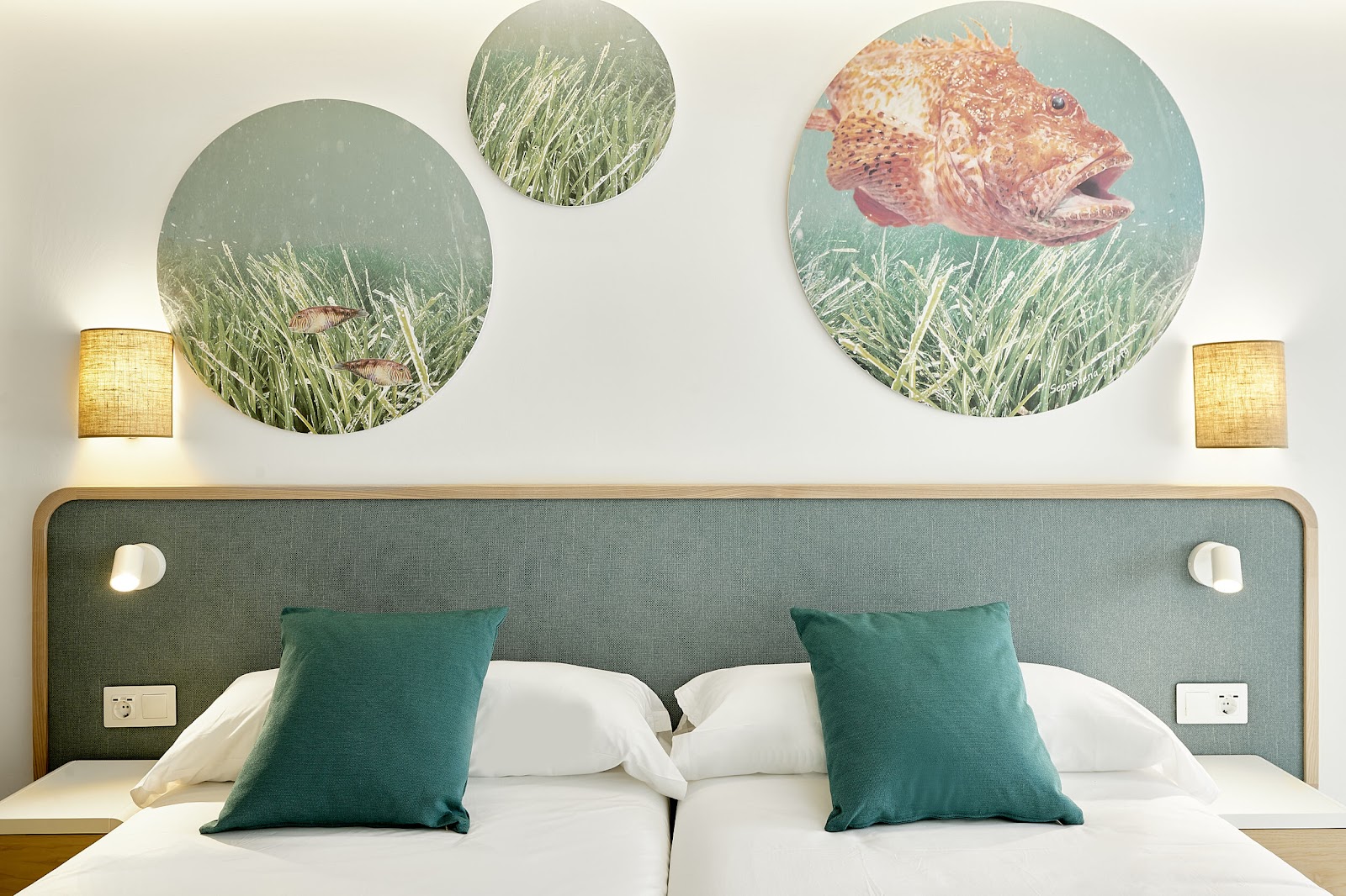 Resort bedroom with green upholstered headboard, white bedding, teal pillows, and circular underwater artwork above the bed.