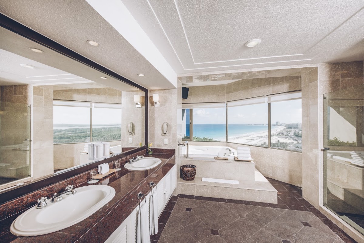 Spacious bathroom with dual sinks, soaking tub, and floor-to-ceiling windows overlooking Iberostar Selection Cancún beach and coastline.