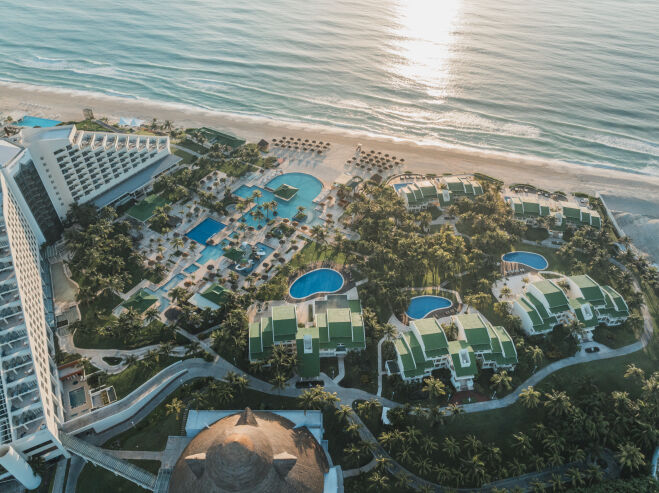 Aerial view of Iberostar Selection Cancún with multiple blue pools, beachfront buildings, lush grounds, and Caribbean Sea beyond.