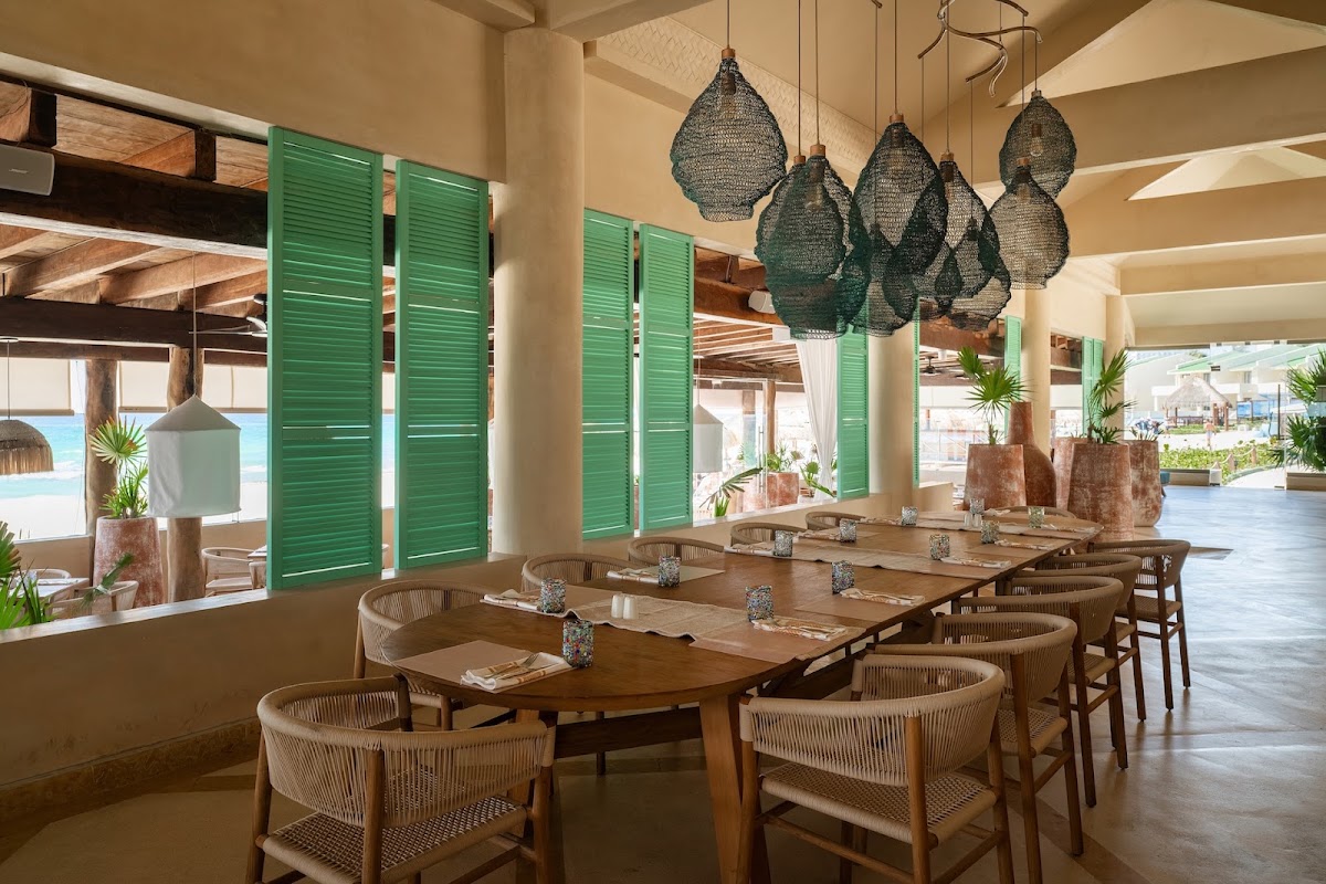 Dining room with wooden tables, woven chairs, woven pendant lights, and green shutters opening to ocean views.