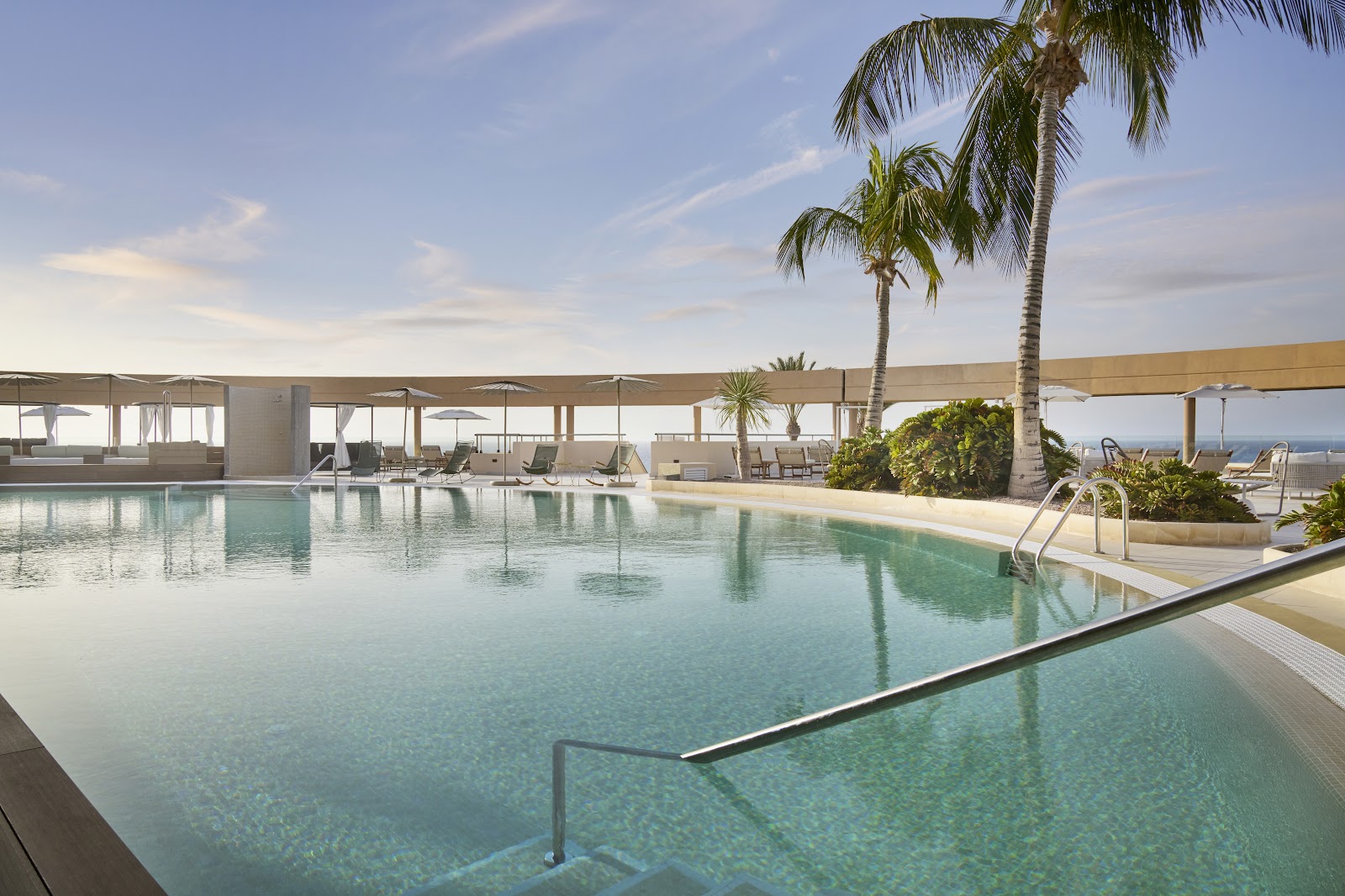 Turquoise pool with lounge chairs and umbrellas at Iberostar Selection Fuerteventura Palace, with palm trees and ocean view.