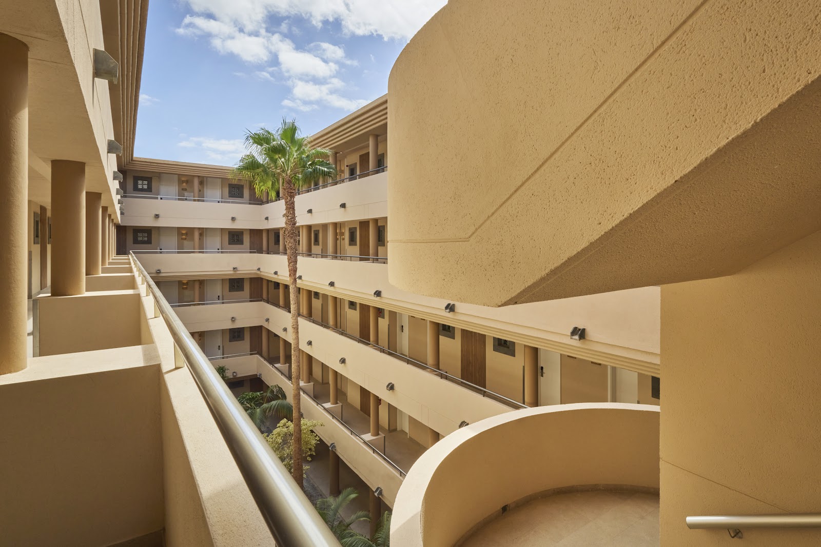 Multi-story beige building with curved balconies surrounding a central courtyard with a palm tree at the Iberostar Selection Fuerteventura Palace.