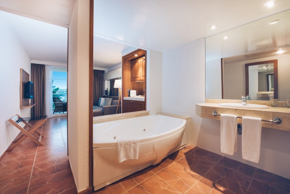 Spacious bathroom with curved soaking tub, dual sinks with wood accents, and ocean view through open doorway at Iberostar Selection Jardín del Sol Suites.