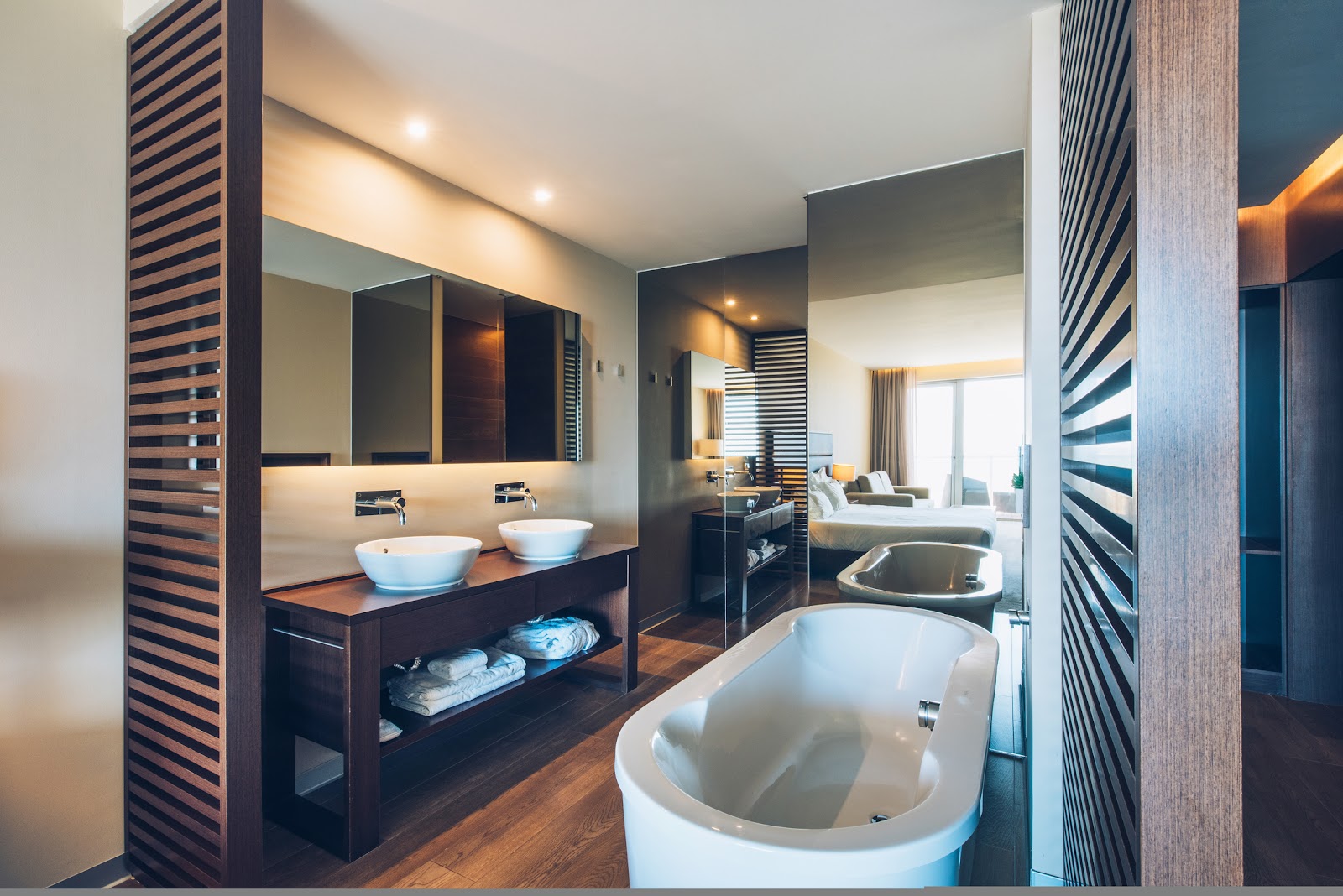 Modern bathroom with freestanding white tub, dual vessel sinks on dark wood vanity, and striped wood partitions at Iberostar Selection Lagos Algarve.