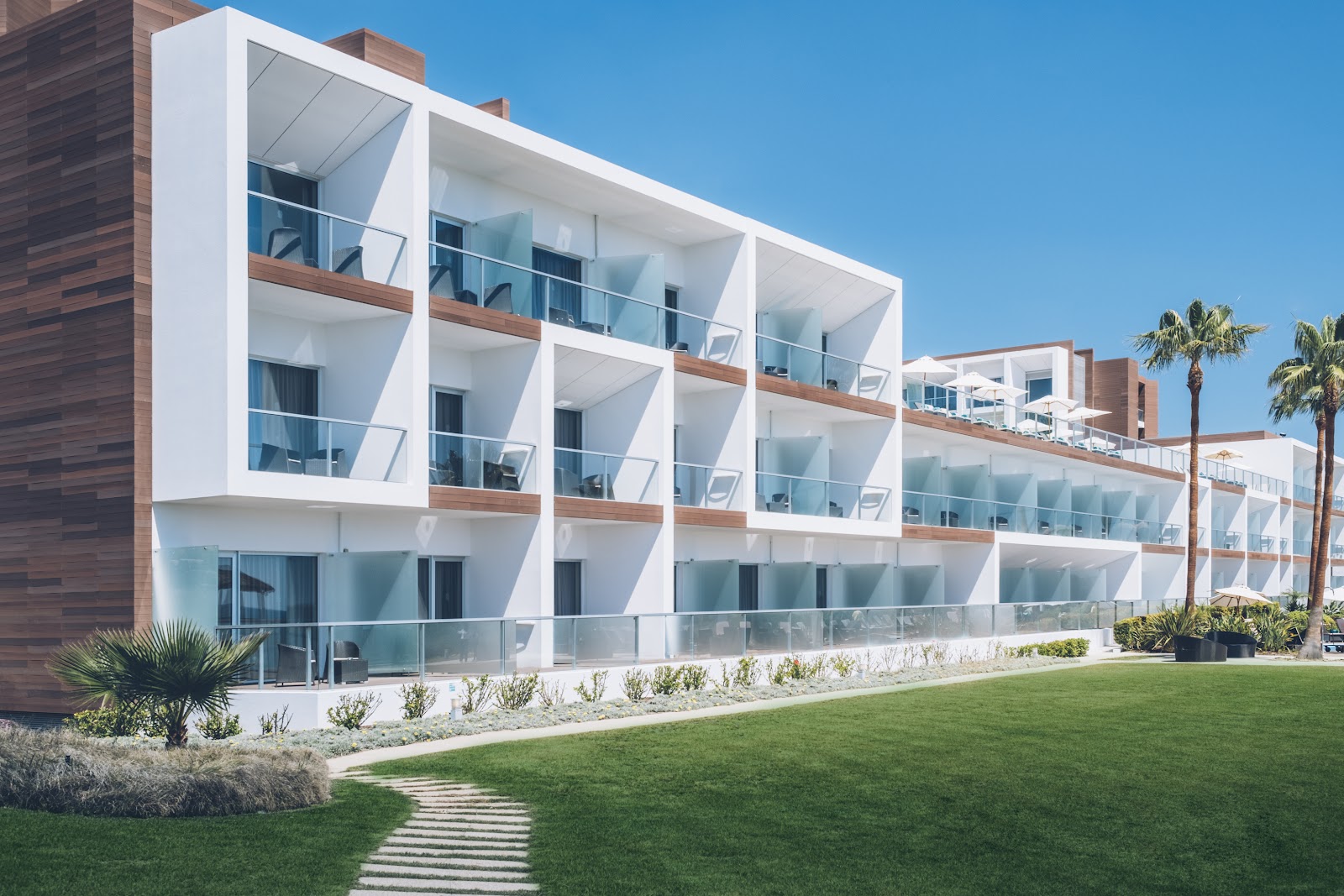 Modern lounge with blue and tan seating, floor-to-ceiling windows overlooking the ocean and beachfront buildings at Iberostar Selection Lagos Algarve.