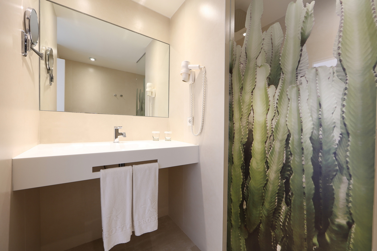 Modern bathroom with white vanity, large mirror, and cactus-print shower curtain at Iberostar Selection Lanzarote Park.