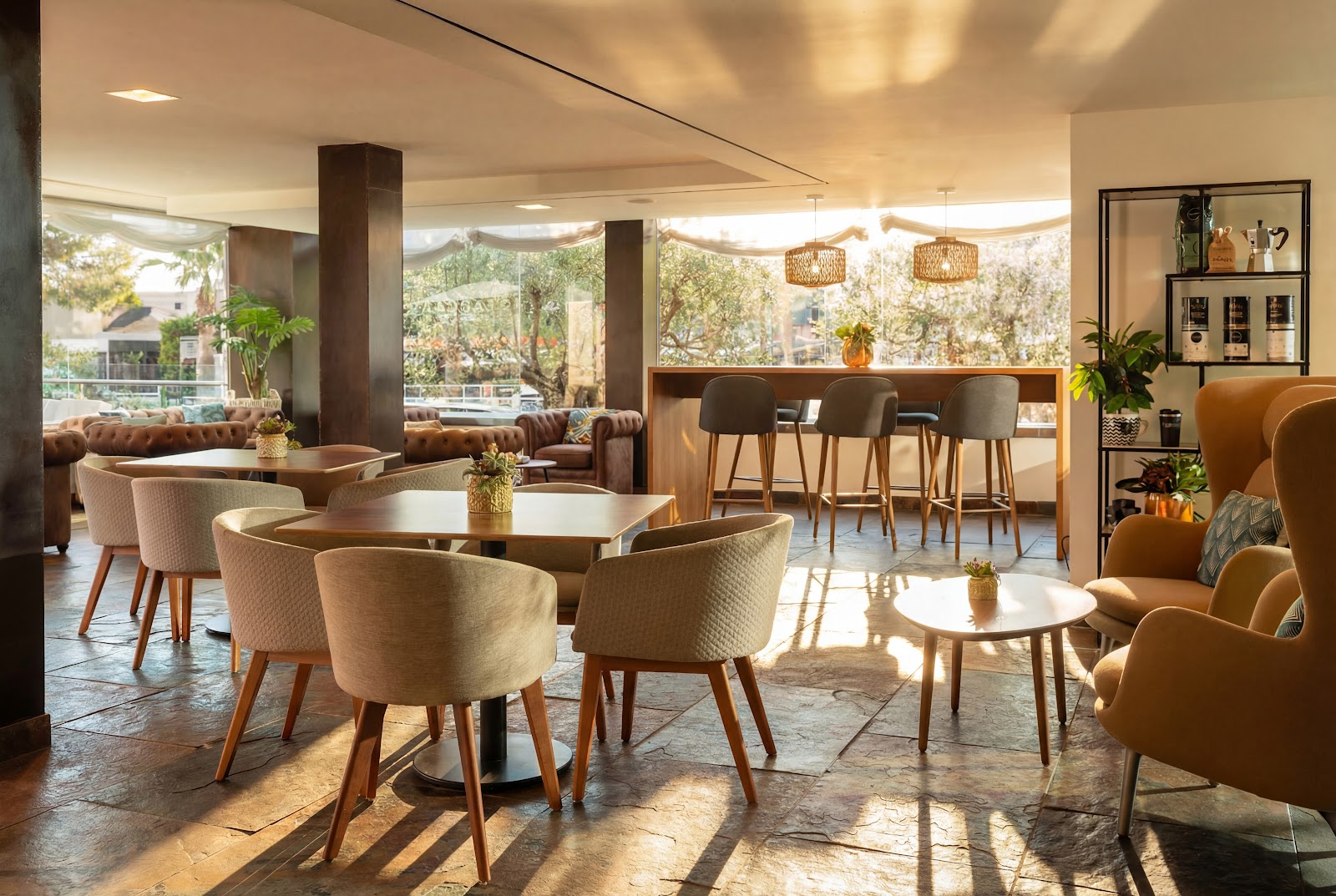 Modern lounge area with cream and tan upholstered chairs around small tables, bar seating, and mountain views through large windows.