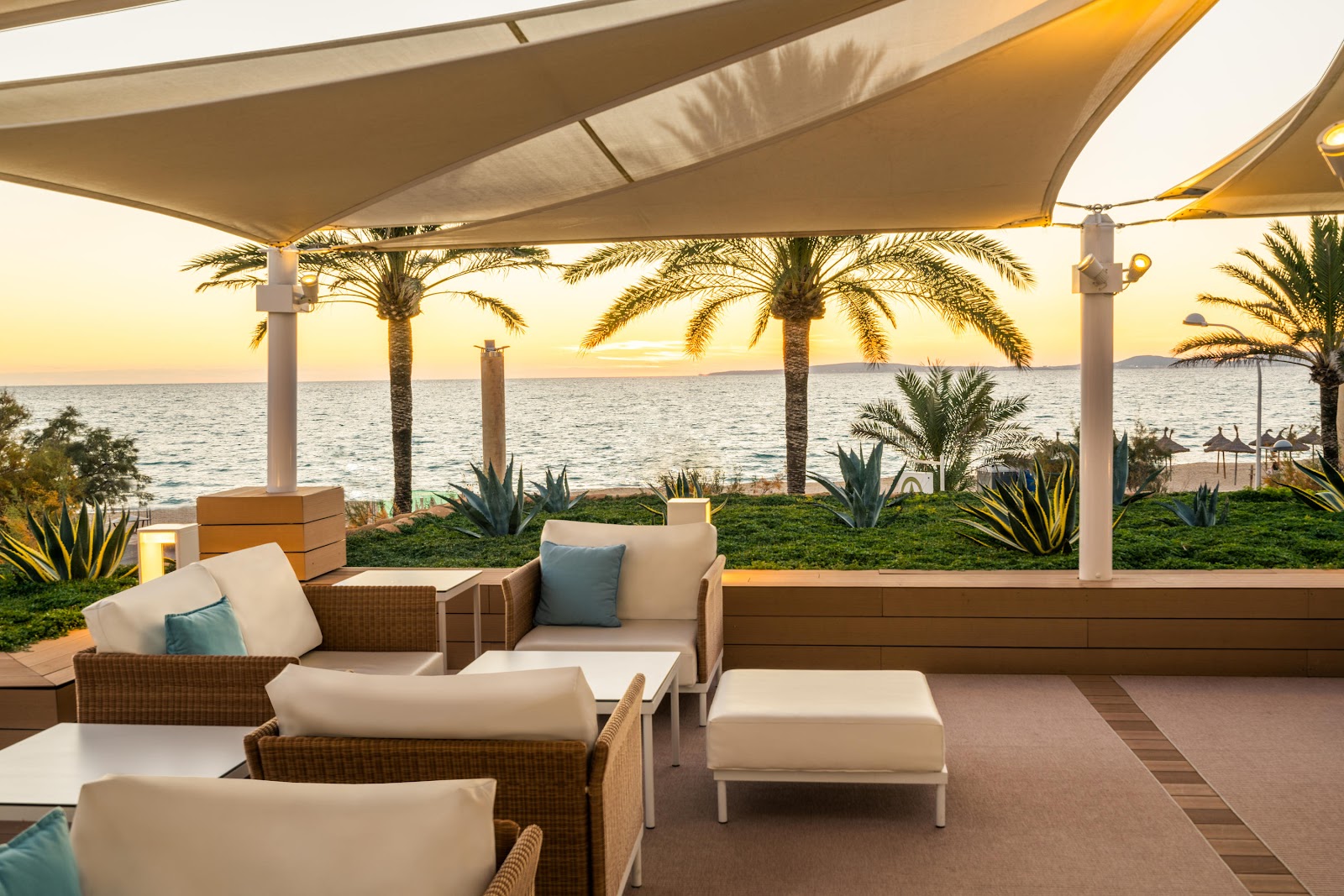 Two guests relax on turquoise lounge chairs under white pergolas beside a resort pool with metal handrail visible in foreground.