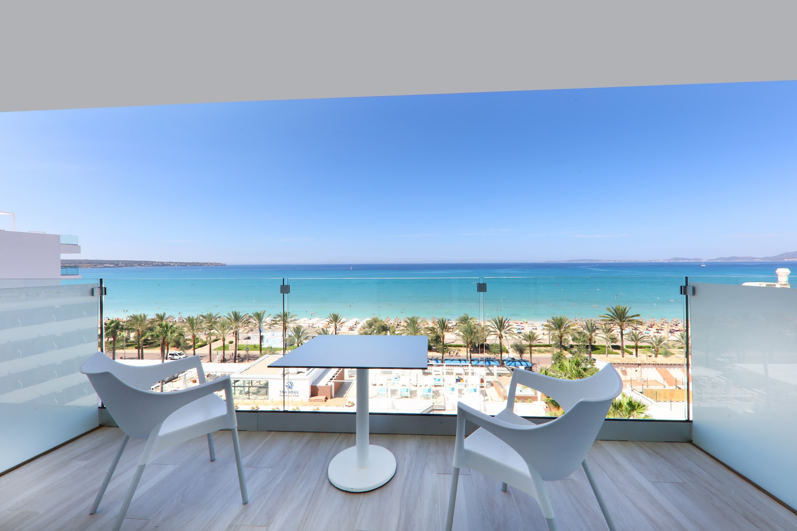 Balcony with two modern chairs overlooking turquoise water, palm-lined beach, and blue sky at Iberostar Selection Playa de Palma.