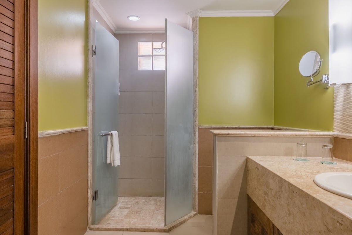 Bathroom with lime green upper walls, tan lower walls, walk-in shower with glass enclosure, and vanity with round mirror.