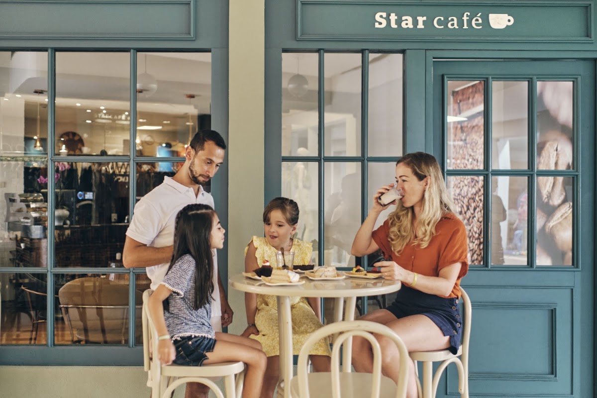 Family of four dining at Star Café with pastries and beverages at a small round table outside the teal-framed storefront.