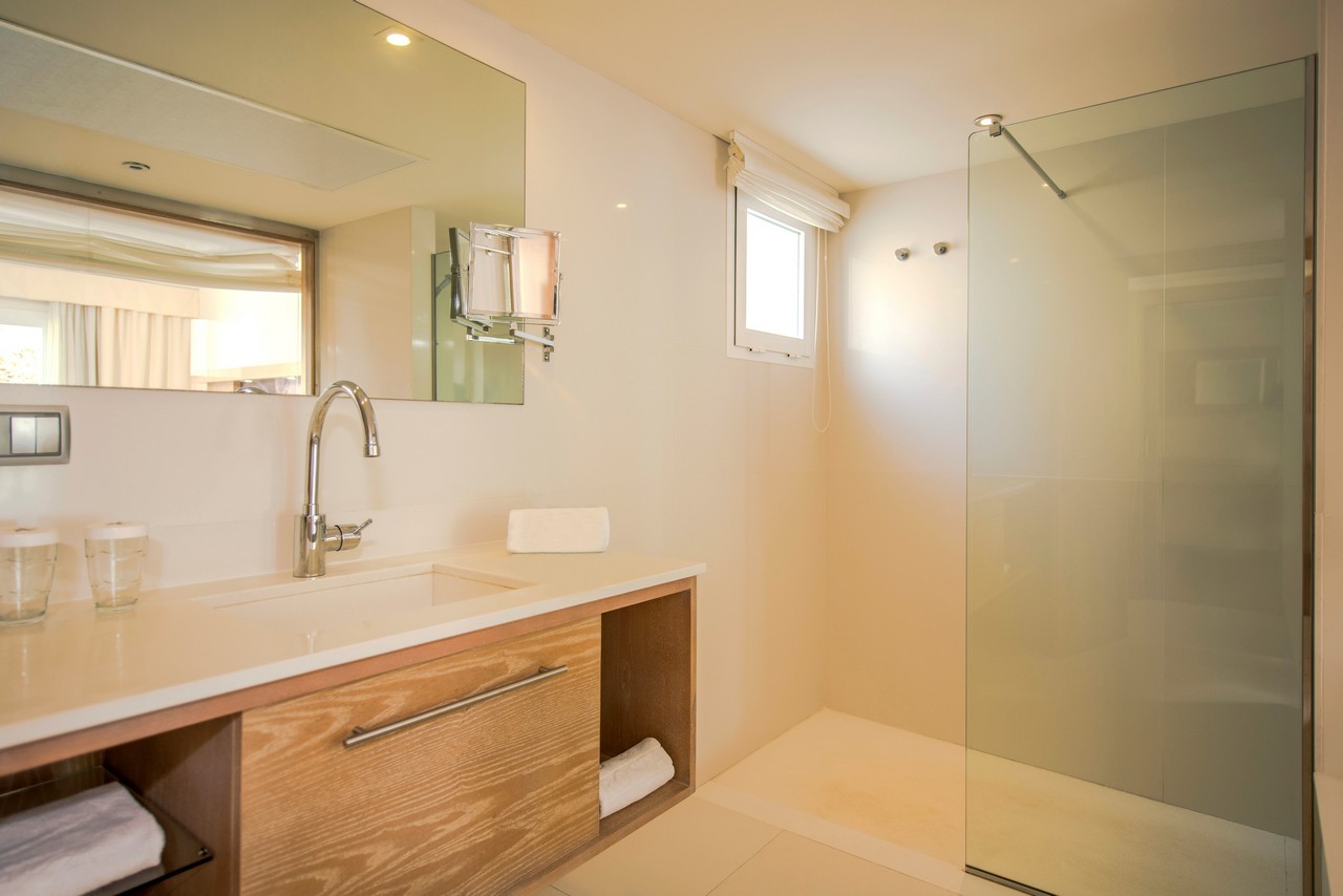 Modern bathroom with wooden vanity, white countertop, large mirror, and walk-in shower with glass enclosure at Iberostar Waves Club Cala Barca.