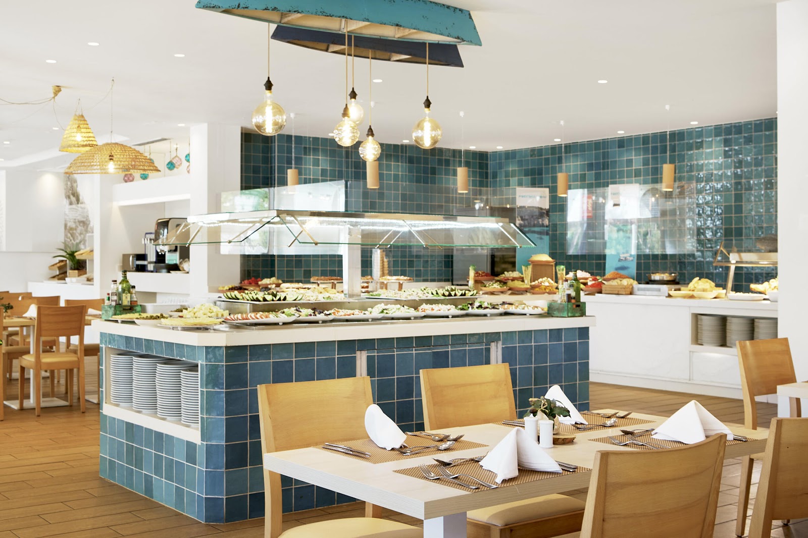 Resort buffet counter with white bowls of colorful dishes under copper heat lamps, windows overlooking the pool area.