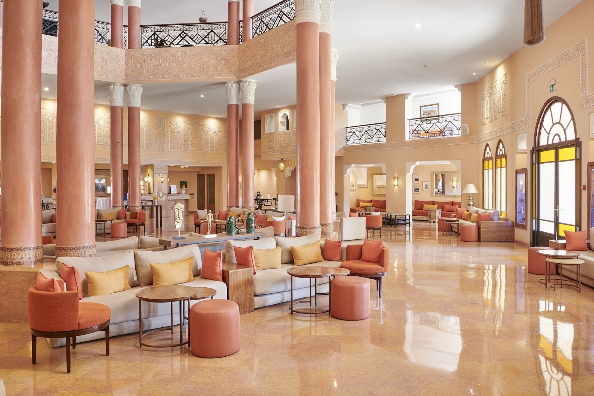 Spacious lobby with coral columns, beige sofas with gold pillows, and arched windows overlooking the atrium at Iberostar Waves Club Palmeraie Marrakech.