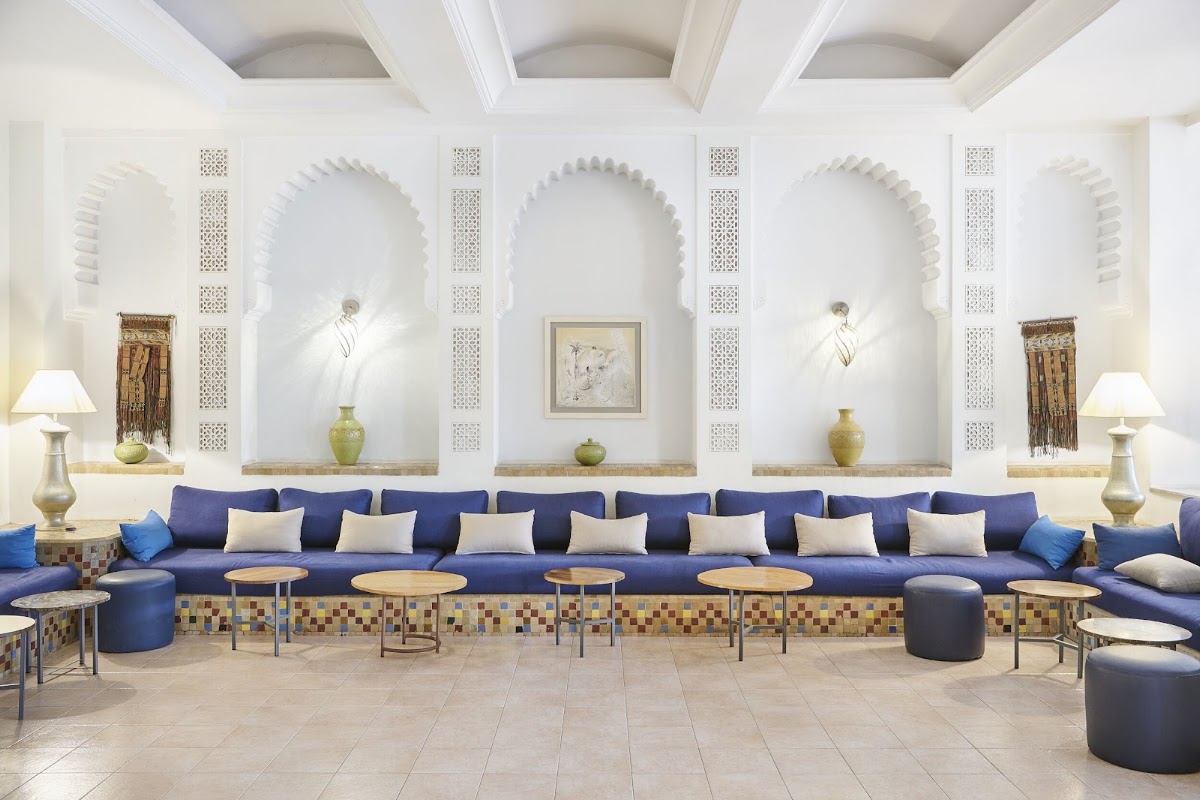 Spacious lobby with a long navy sectional sofa, Moroccan arched alcoves, geometric tile details, and brass accent tables beneath a coffered ceiling.