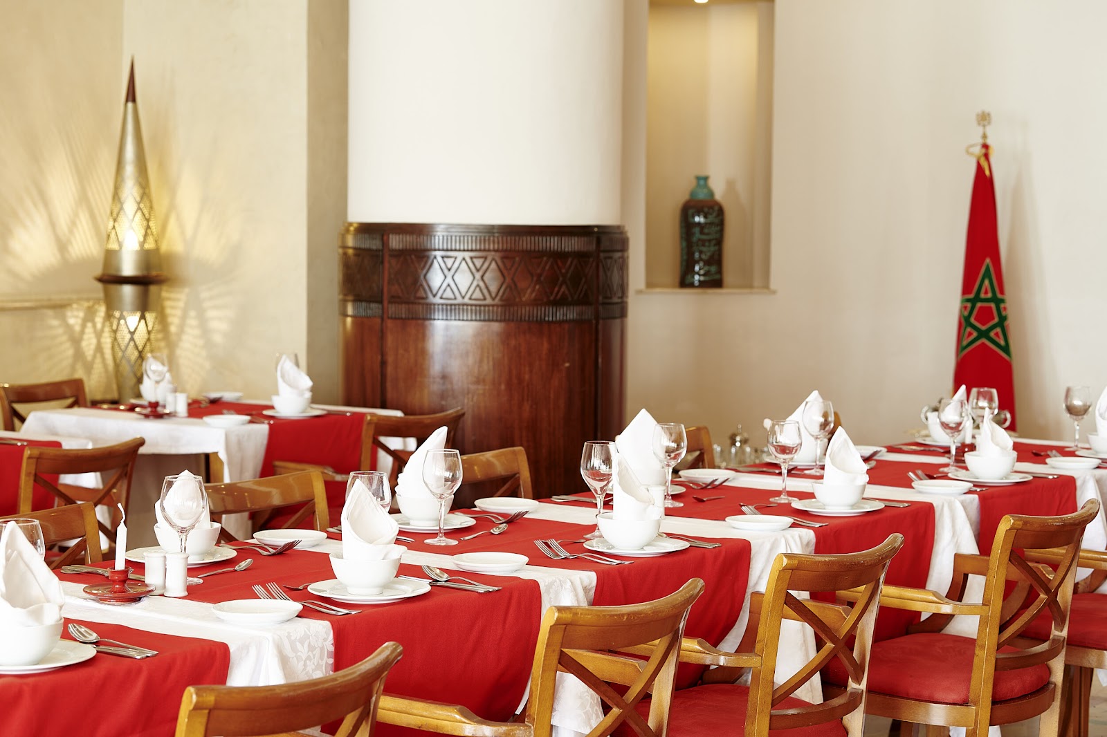 Elegant dining room with red tablecloths, white napkins, wooden chairs, and a Moroccan flag on display.