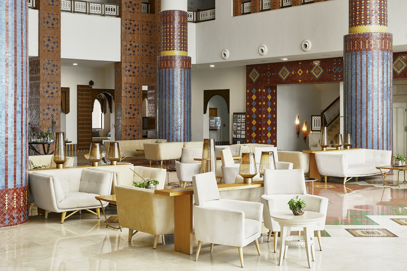 Spacious lobby with cream armchairs, brass accents, and tall decorative columns with geometric patterning in earth tones and blue stripes.