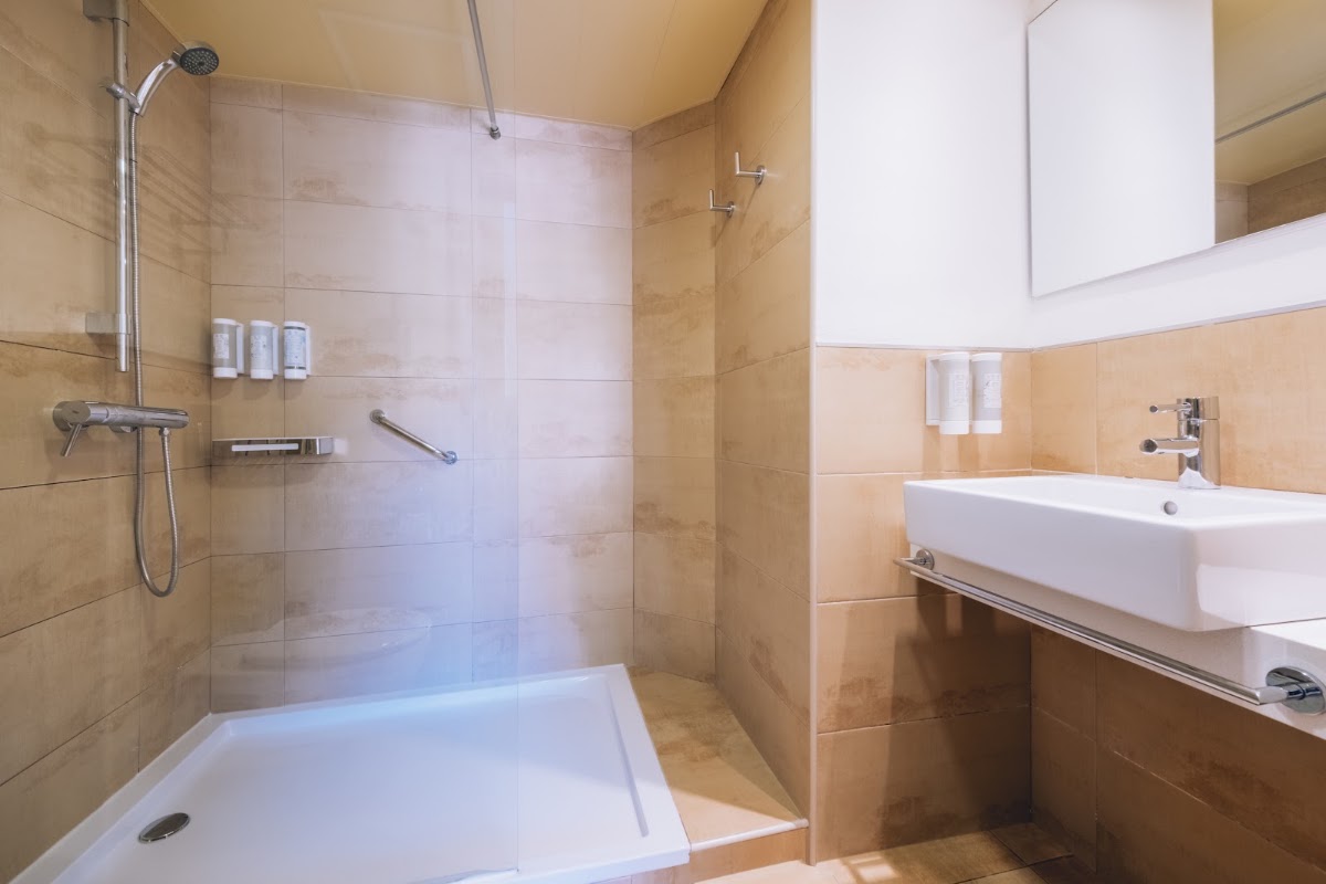 Modern bathroom with beige tile walls, walk-in shower with glass enclosure, white vessel sink, and overhead skylight at Iberostar Waves Pinos Park.