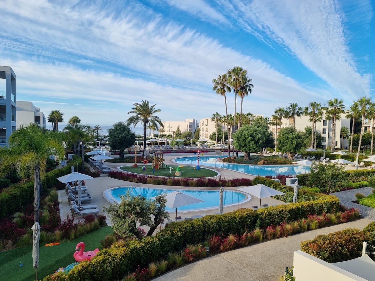 Multiple curved pools with blue water surrounded by palm trees, loungers, and manicured gardens at Ikos Andalusia resort.