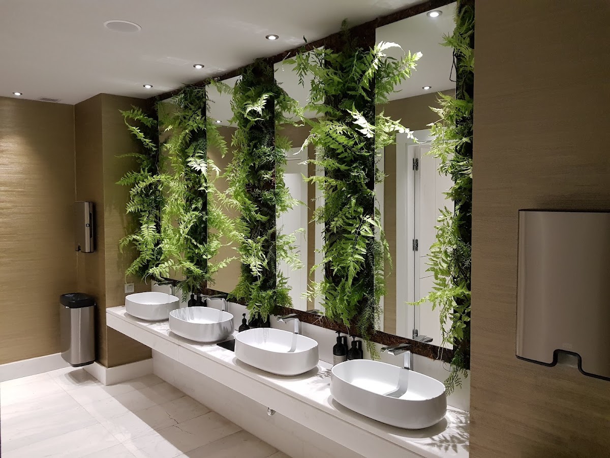 Modern bathroom with four white oval sinks along a counter beneath a large mirror, flanked by lush green living plant walls and recessed lighting.