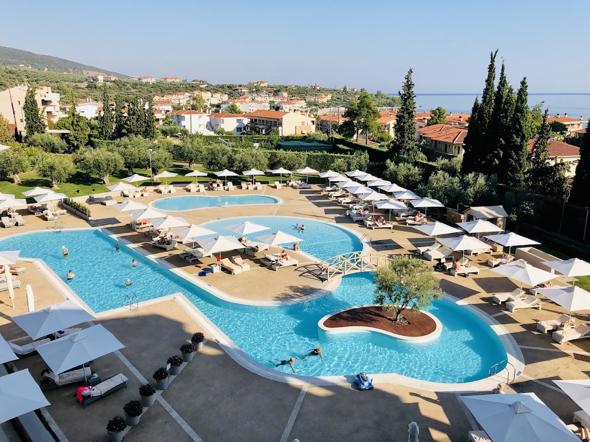 Multiple pools with white umbrellas and loungers overlook a Mediterranean coastal town and sea at Ikos Olivia.