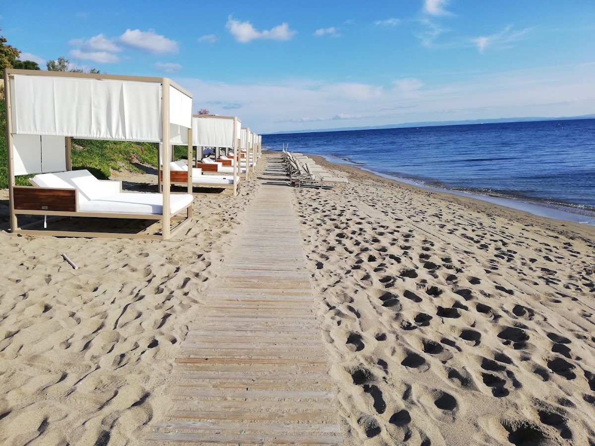 Wooden boardwalk lined with white cabana beds leading to a sandy beach and blue sea at Ikos Olivia.