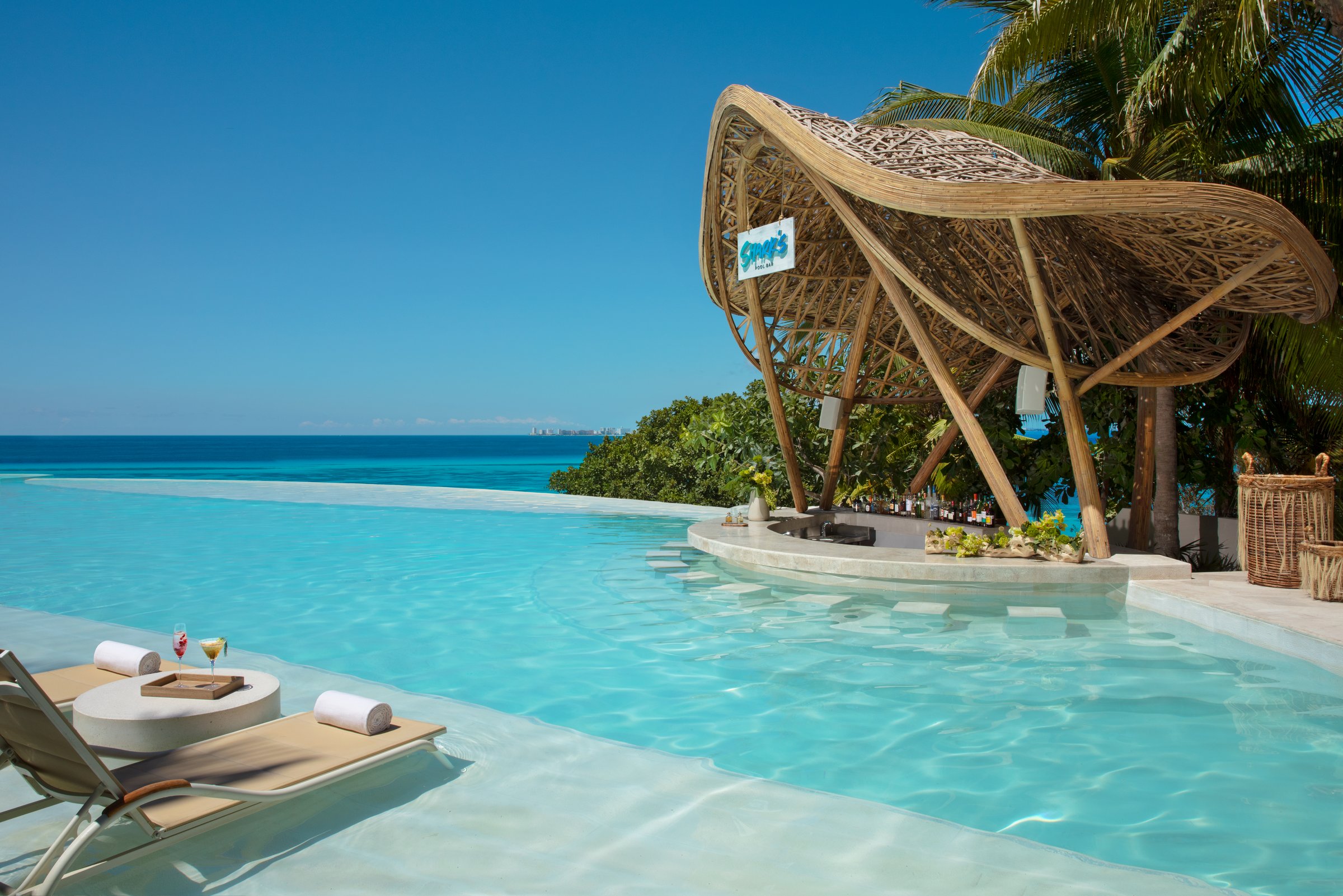 Sharks swim-up bar under a large modern thatched roof beside the infinity pool, with the sea beyond.