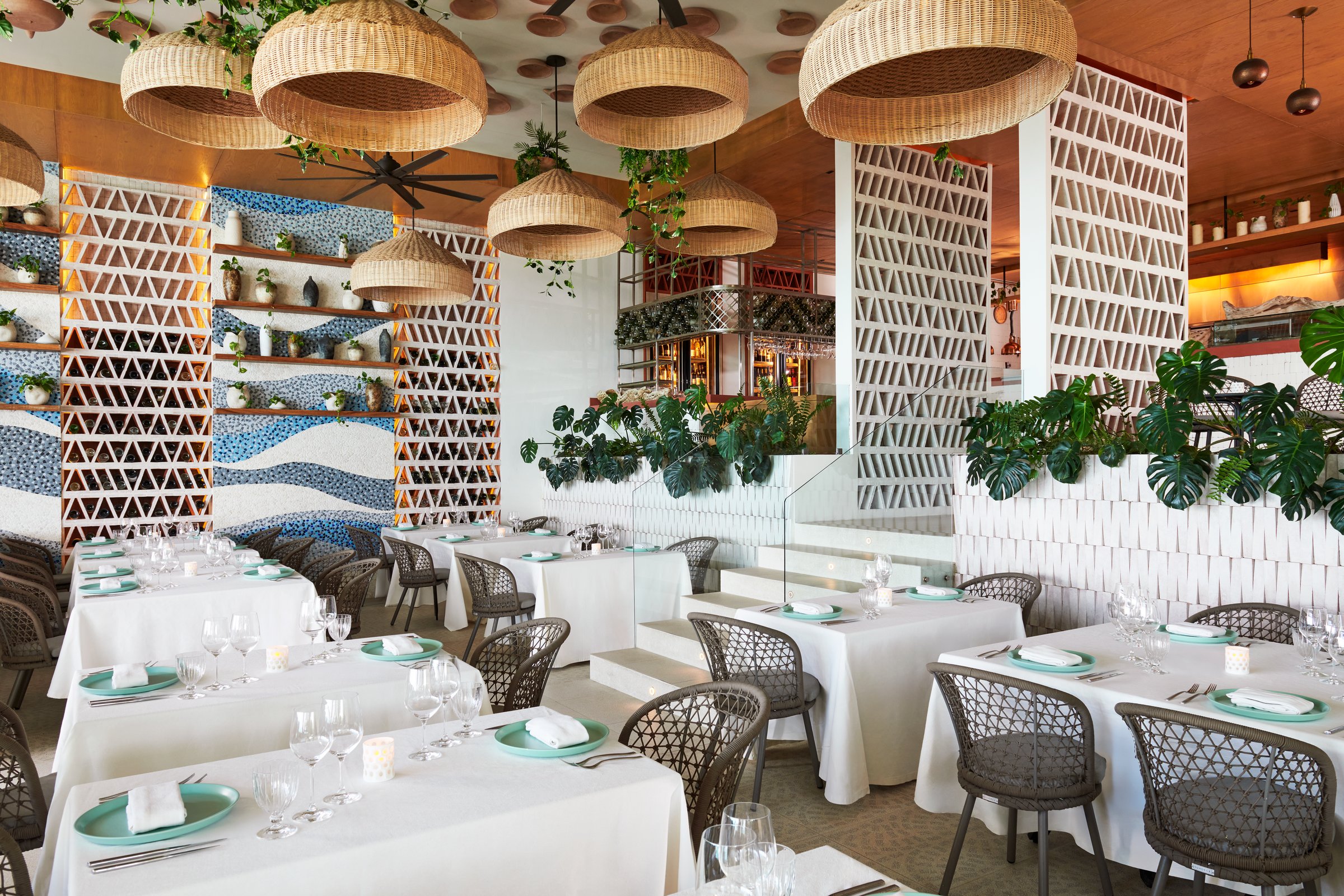 Spezia dining room with white linen tables, woven gray chairs, hanging wicker lights and white lattice partitions.