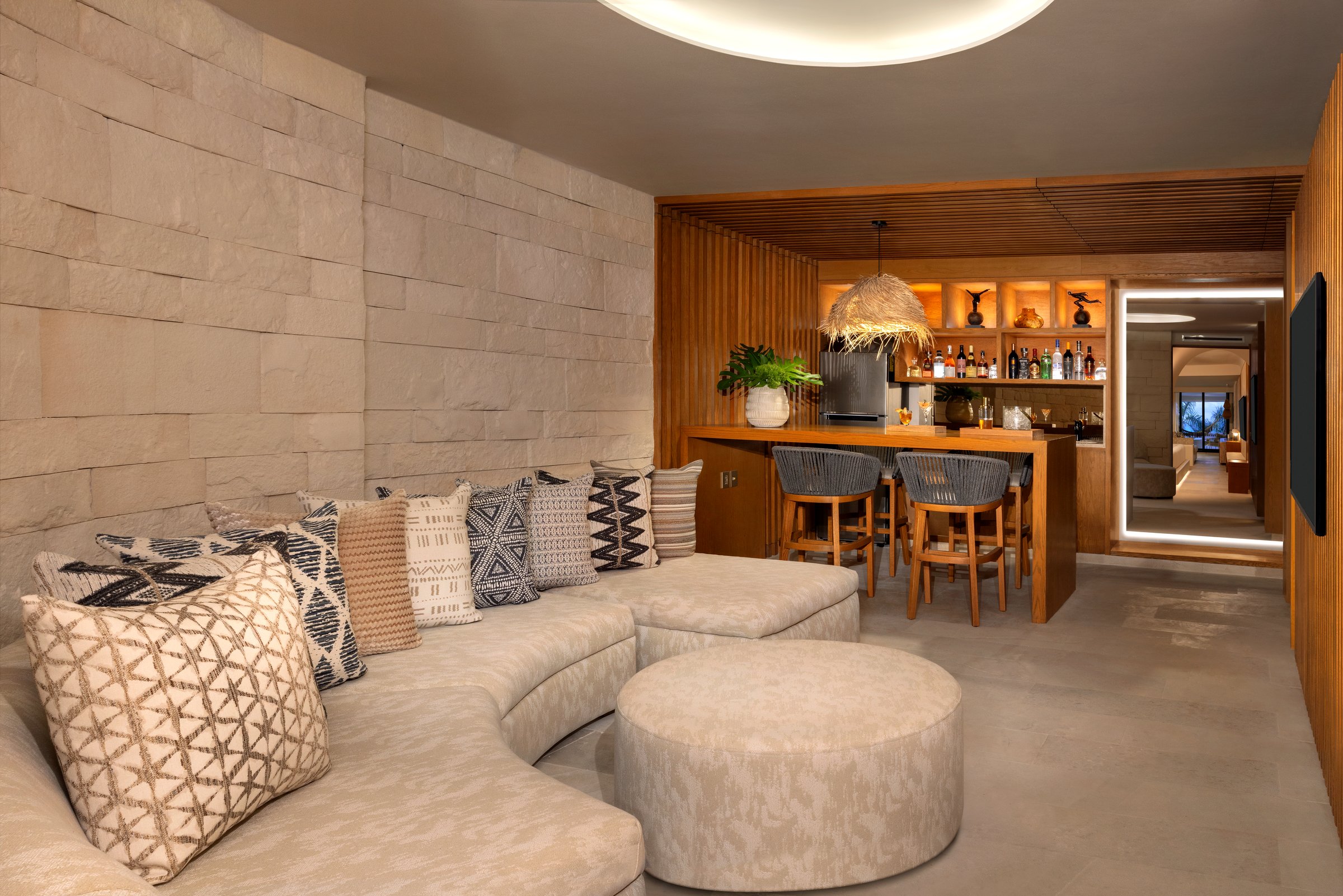 Paramount suite living room with a curved beige sectional, light stone wall and a warm wood bar area.