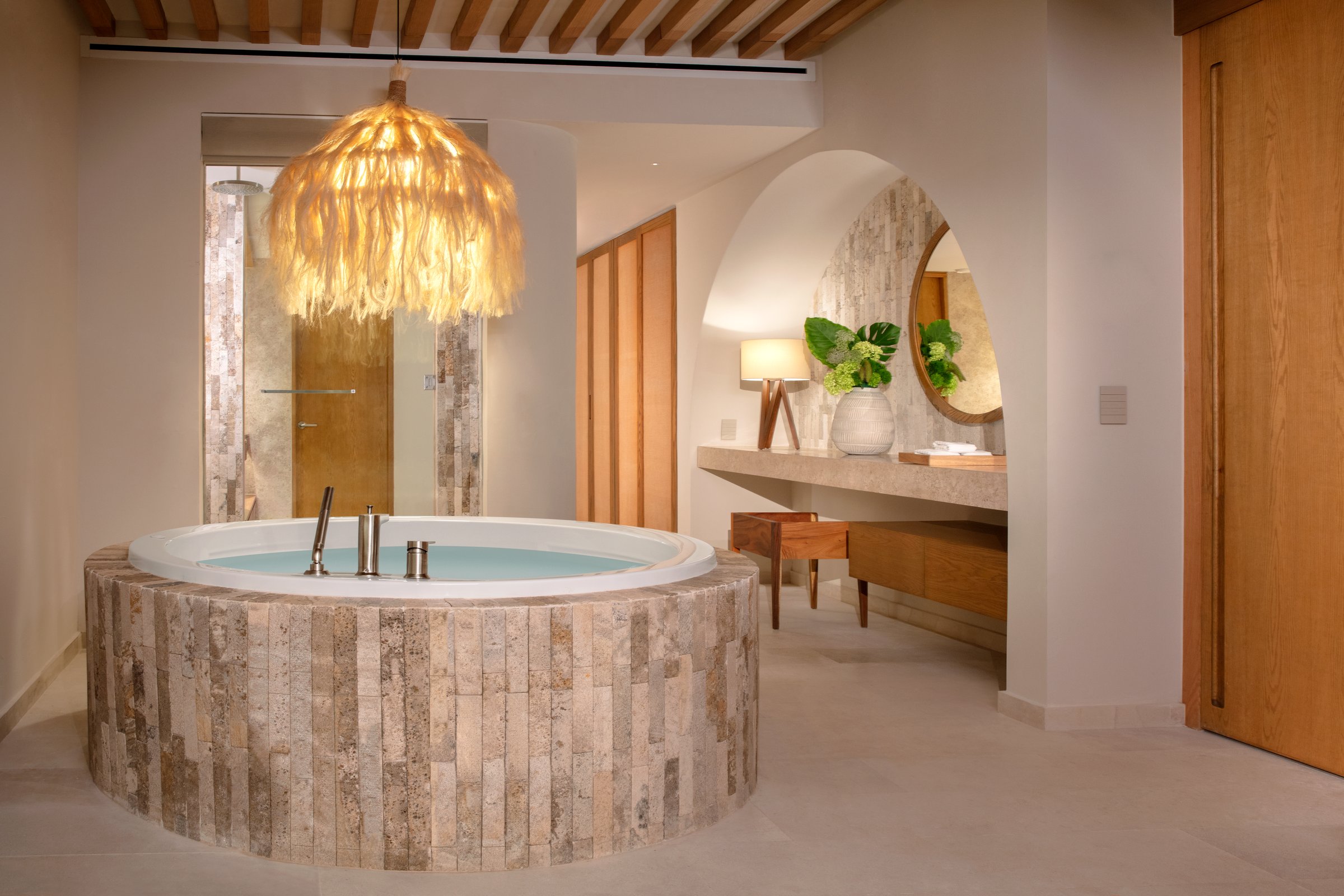 Presidential suite bathroom with a large round stone-encased soaking tub under a woven pendant light.