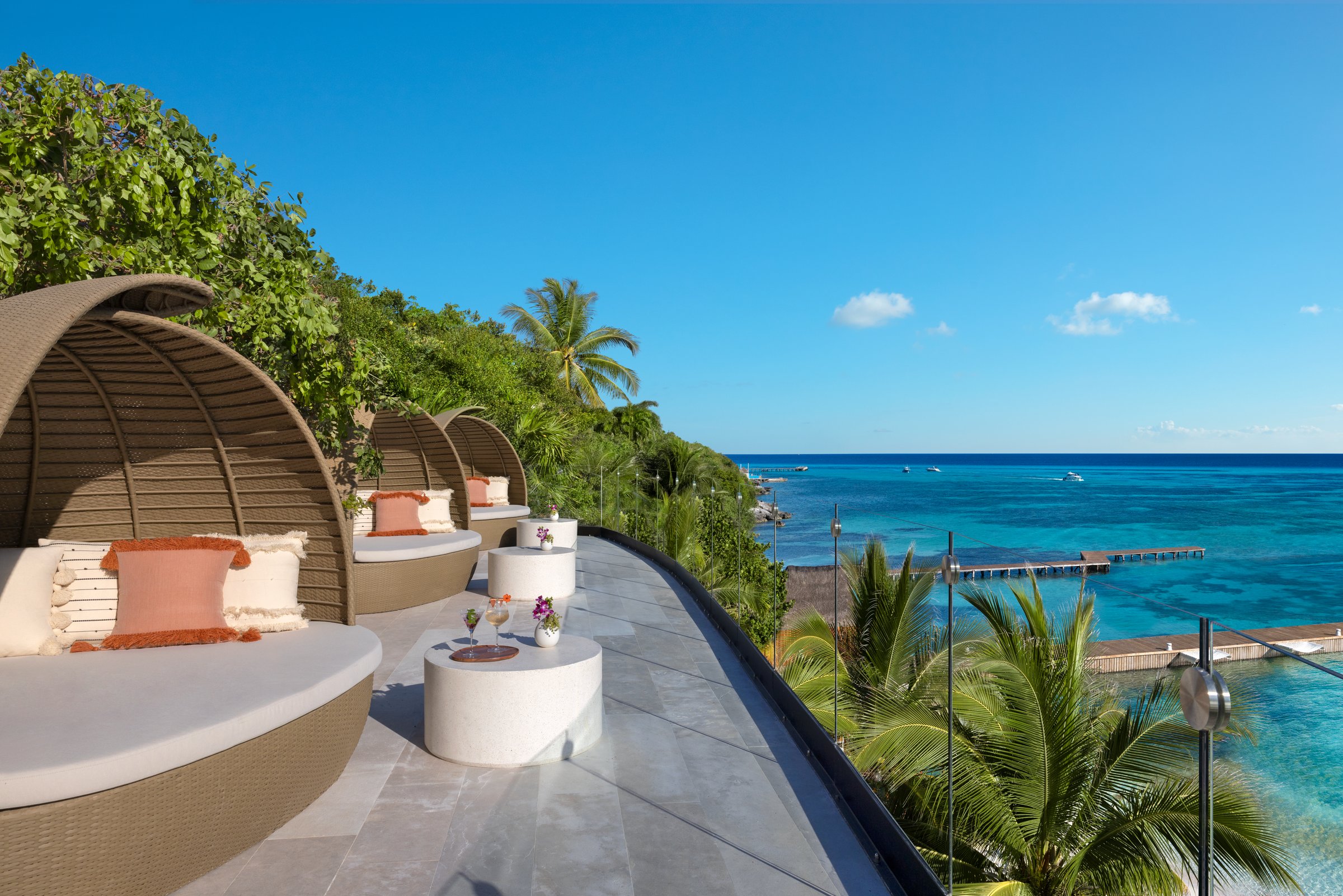 Barecito terrace over the turquoise sea with round wicker lounge pods and white cushions.