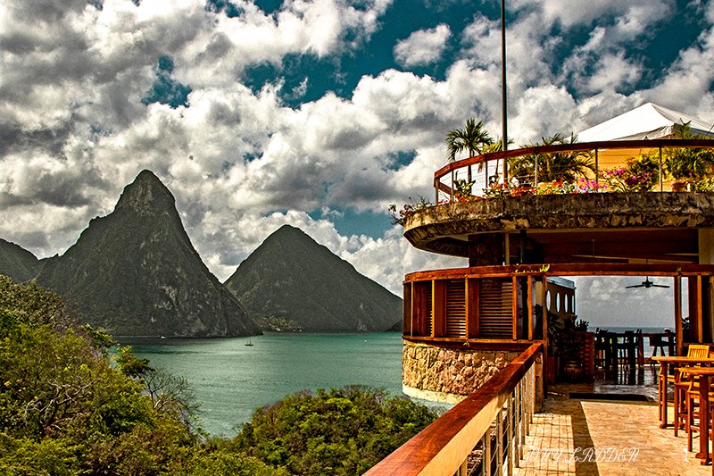 Wooden terrace with dining area overlooking turquoise bay and iconic green peaks under cloudy sky at Jade Mountain.