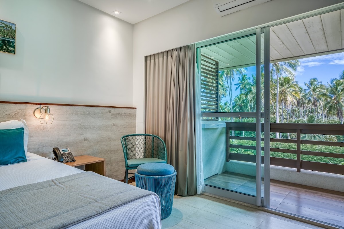 Resort bedroom with sliding glass doors opening to a balcony overlooking palm trees and ocean view.