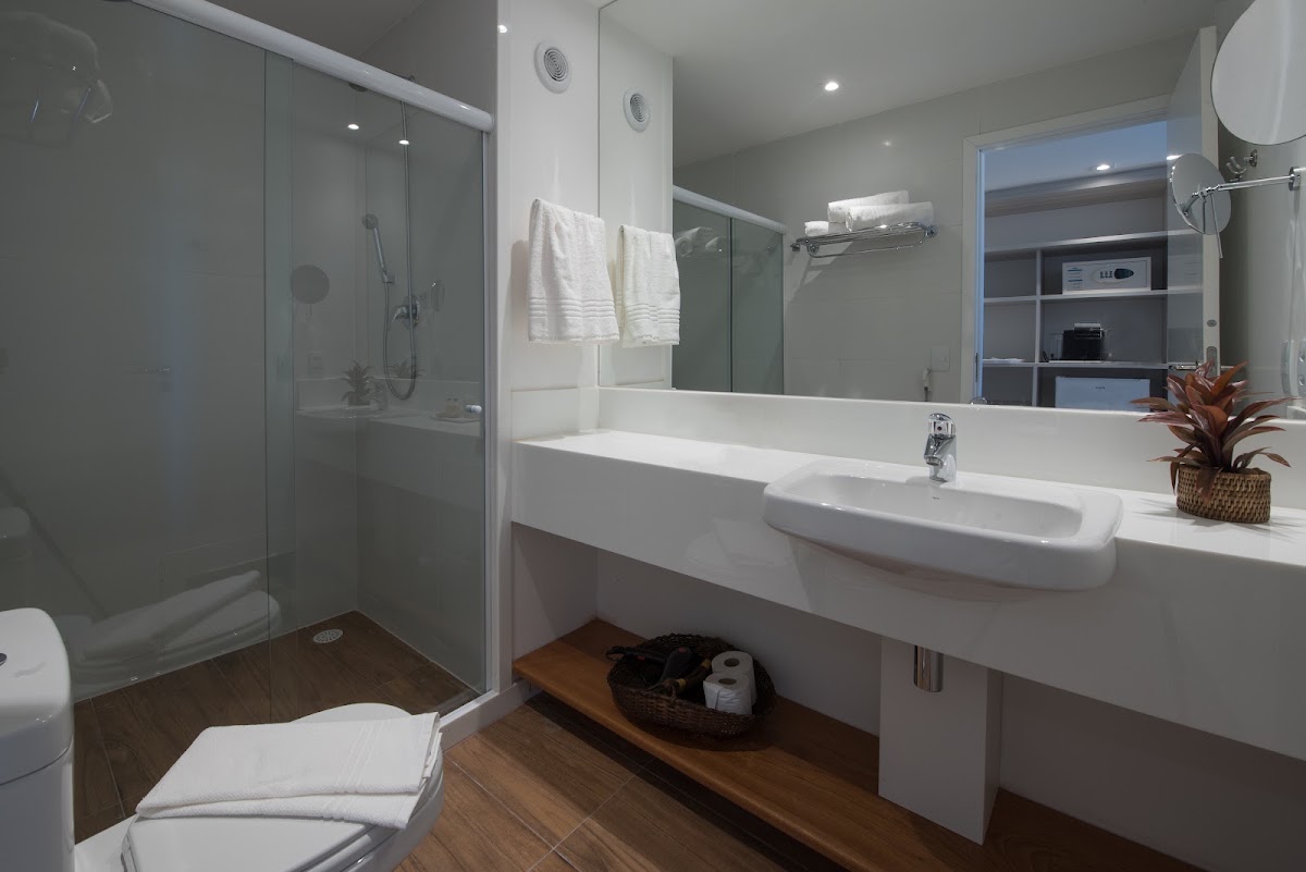 Modern bathroom with white dual sink vanity, glass shower enclosure, and wood flooring at Japaratinga Lounge Resort.